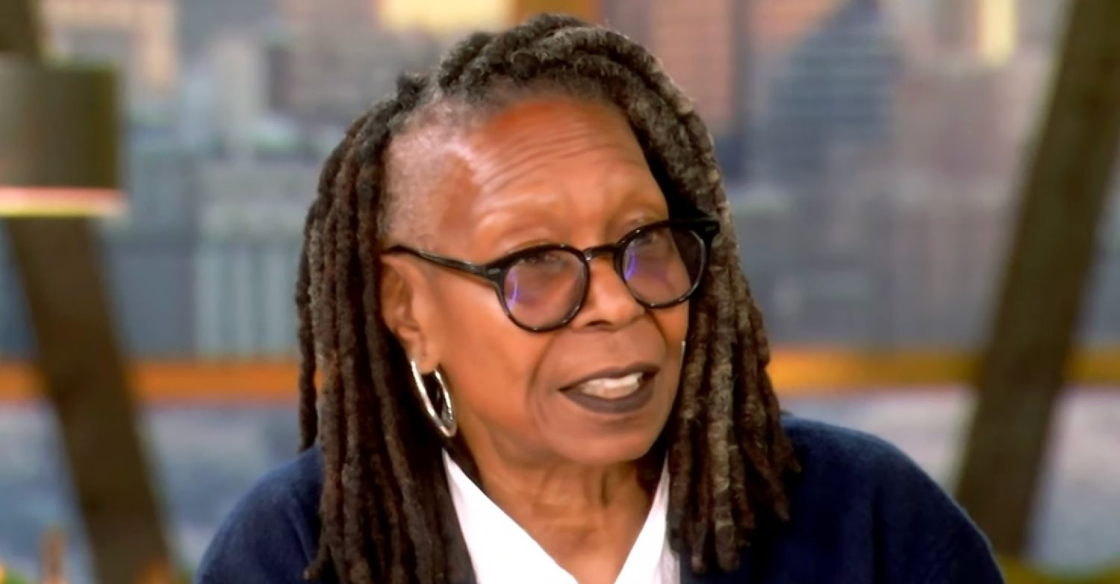 Whoopi Goldberg wearing the black Some Days Are Trickier Than Others unisex zip-front hoodie with white IWBC embroidery on the left chest, oversized fit, and silver zipper, styled casually on The View set, February 2026.