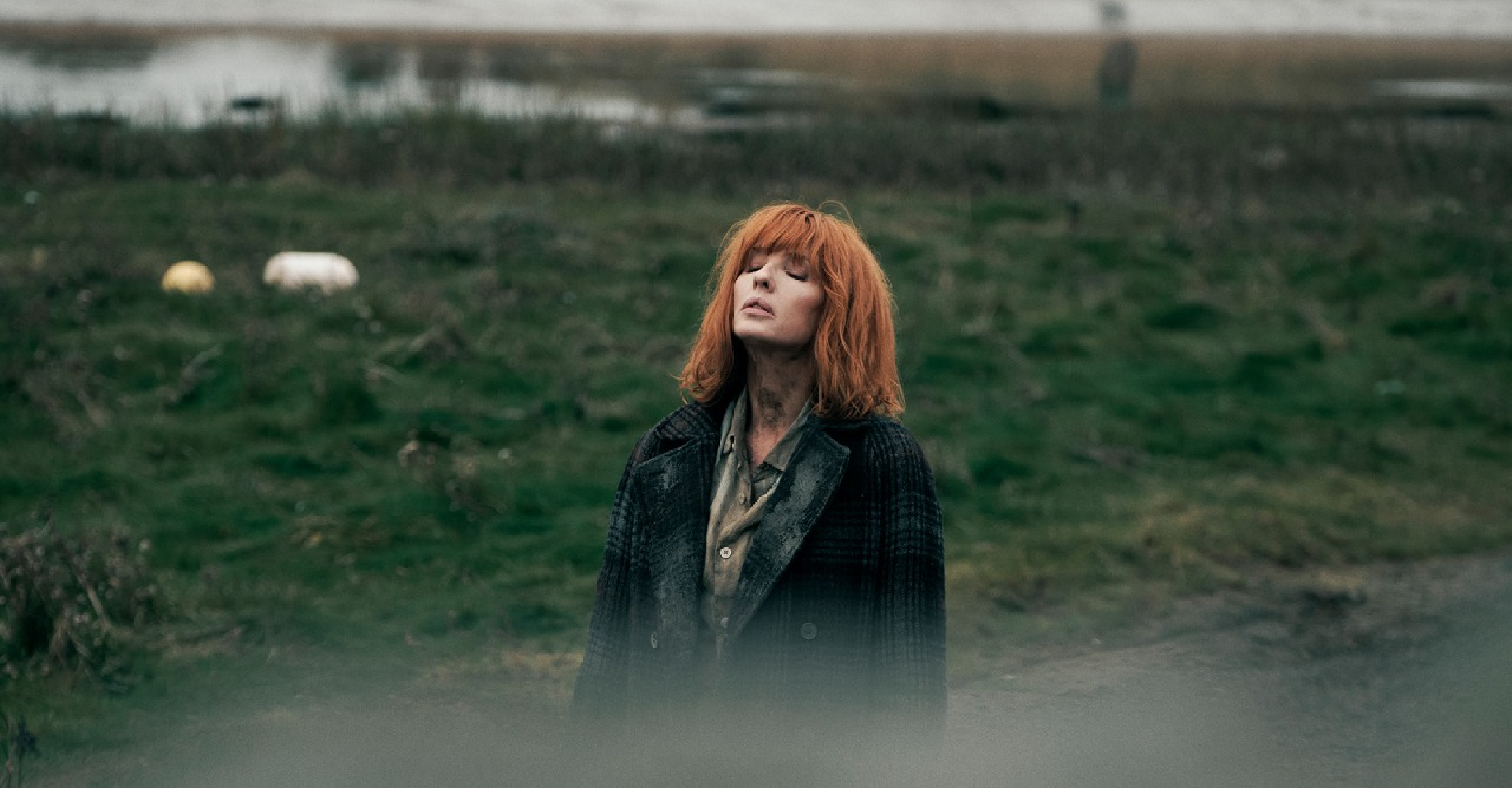 Kelly Reilly wearing the Under Salt Marsh S01 oversized quilted coat in muted olive green, featuring a cream faux shearling lining, tan leather trim on cuffs and pockets, mid-thigh length, and a relaxed, boxy fit.