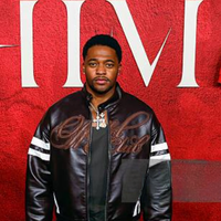 HIM Premiere star Christopher Meyer wears a dark brown leather bomber jacket with white sleeve stripes, adding bold sophistication to the red carpet.