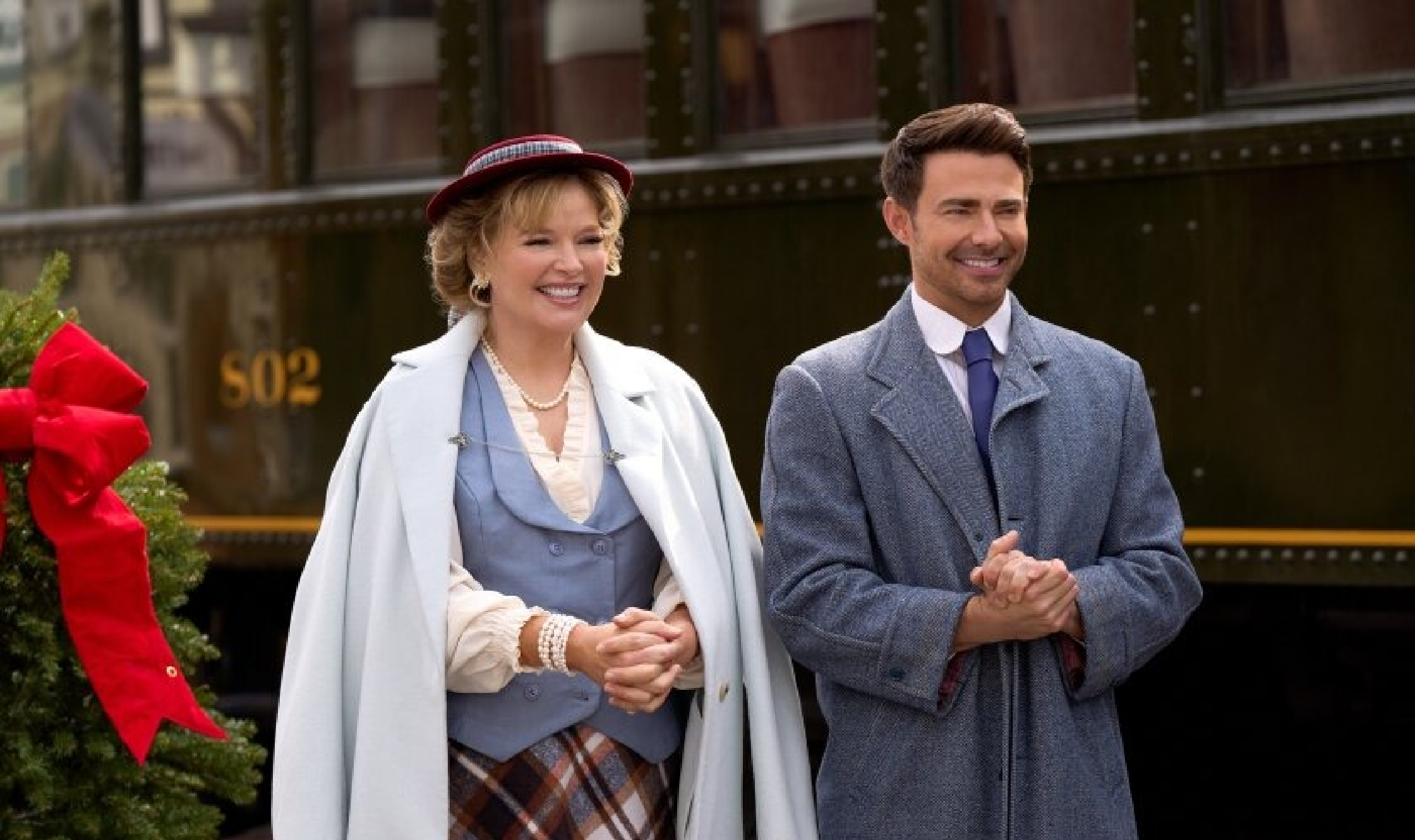 Melissa Peterman wearing a soft periwinkle blue double-breasted tailored vest with rounded shawl lapels and pointed hem, layered over a cream ruffled blouse and styled under a pale blue wool cape coat in Finding Mr Christmas Season 2, Episode 8