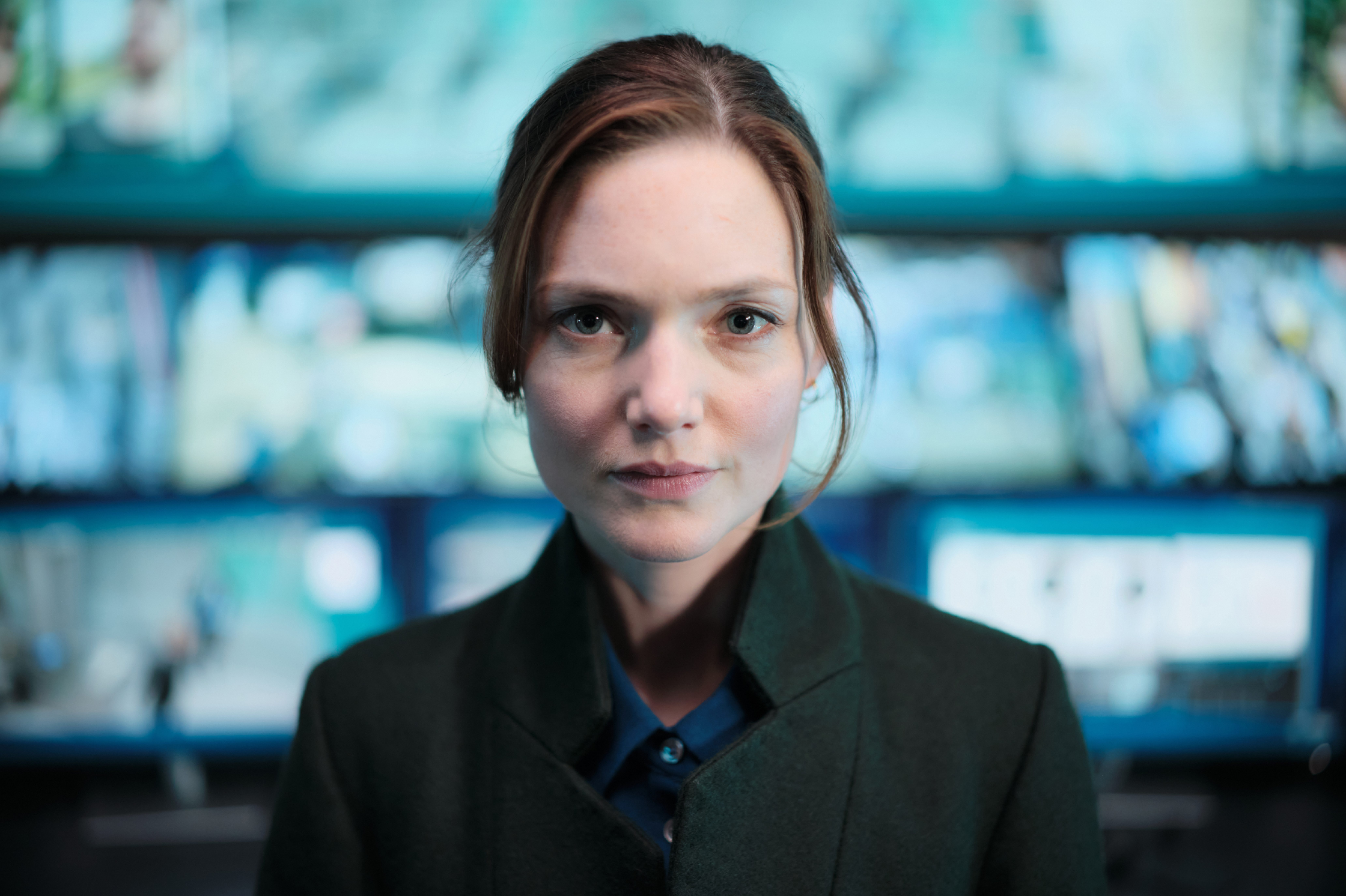 Holliday Grainger The Capture Season 3 forest green wool overcoat with funnel collar and half-belt back, featuring structured A-line silhouette and open-front duster style.