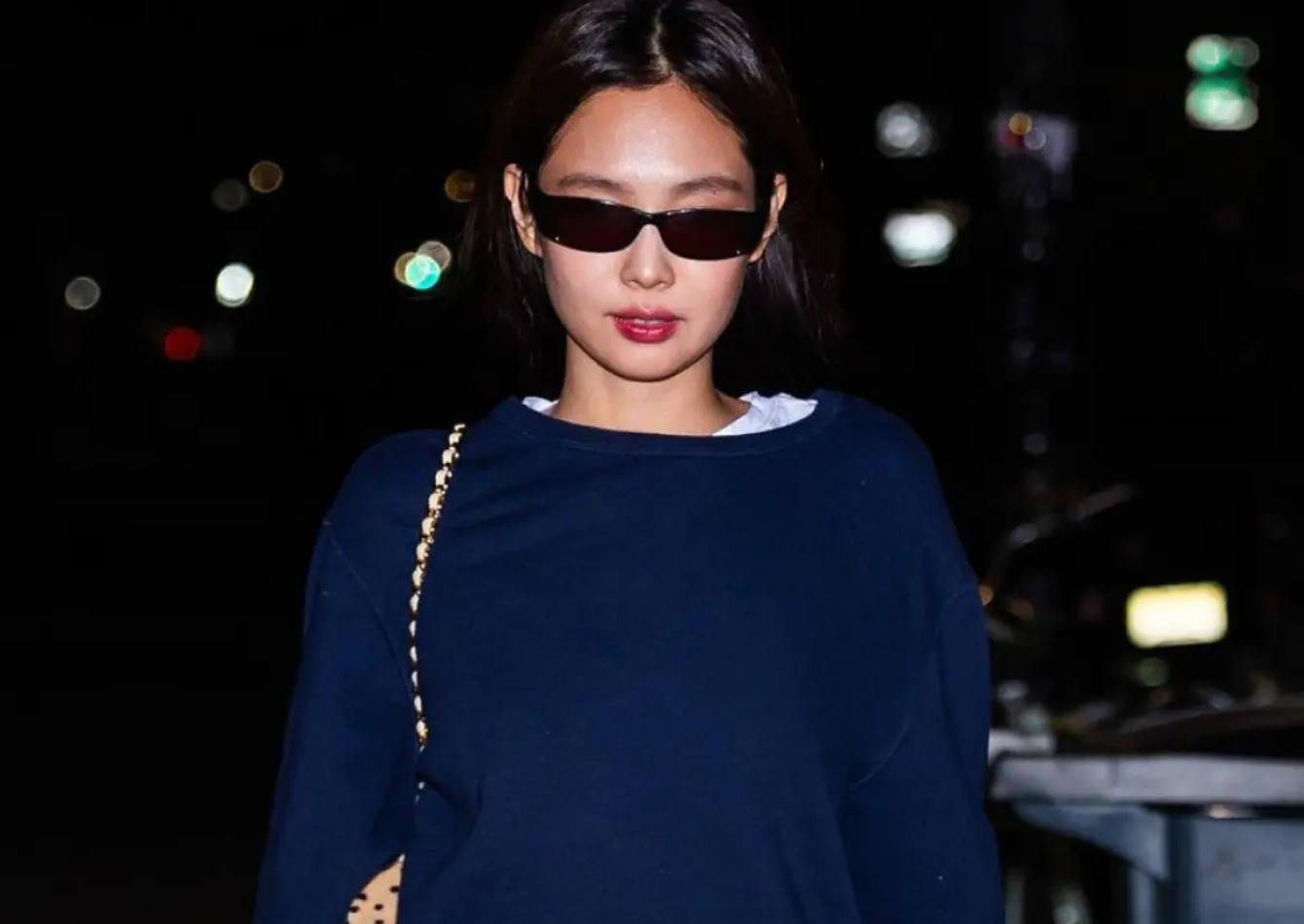 Jennie Kim wearing navy Ralph Lauren crewneck sweatshirt with pinstriped trousers, black sunglasses, and cream quilted shoulder bag in SoHo New York City 2026