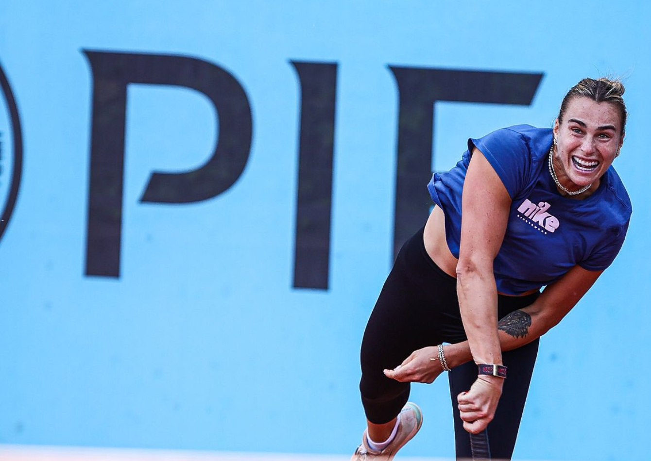 Aryna Sabalenka wearing a royal blue Nike cropped t-shirt, black leggings, and white tennis shoes during Mutua Madrid Open 2026 match on clay court