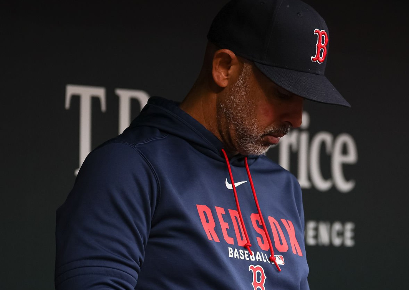 Alex Cora wearing a navy Boston Red Sox Nike pullover hoodie with red lettering and team logo during a dugout game against the Baltimore Orioles
