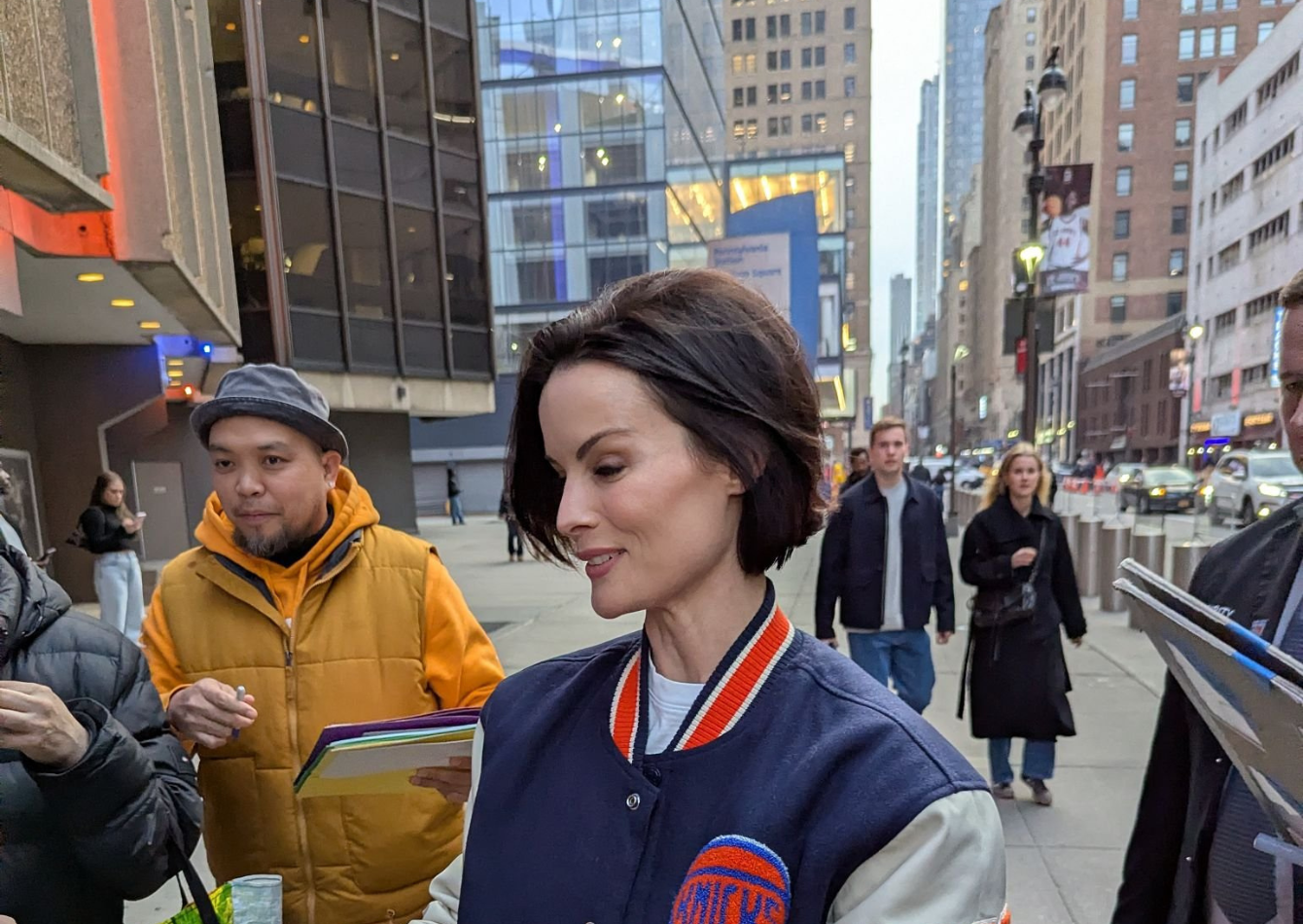 Jaimie Alexander wearing a New York Knicks varsity bomber jacket with navy body, cream sleeves, and large embroidered Knicks logo at Madison Square Garden NYC 2026