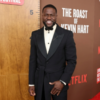 Kevin Hart wearing a black belted tuxedo blazer with oversized satin peak lapels, floral bow tie, and tailored formal styling at The Roast of Kevin Hart red carpet event.