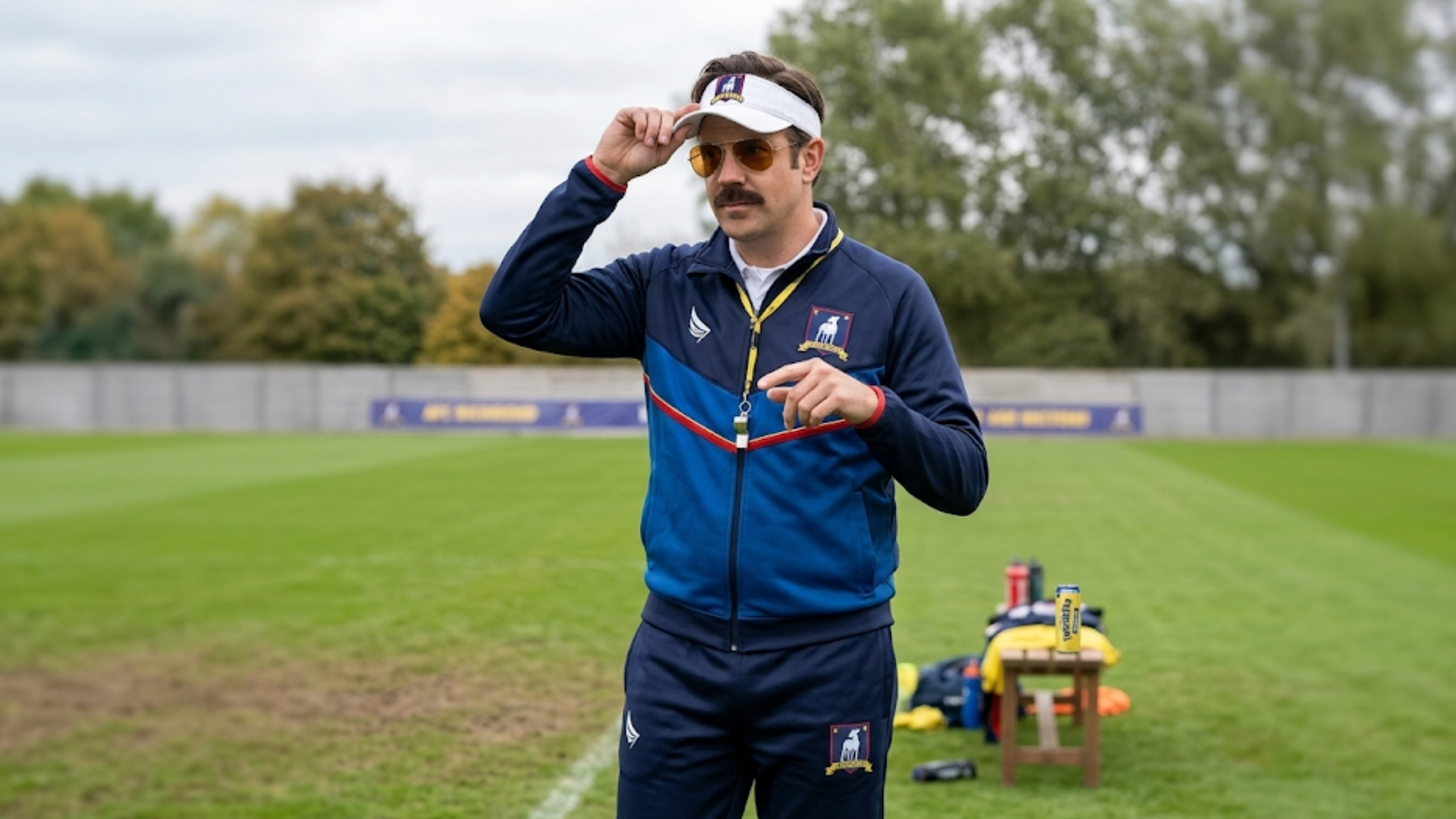 Ted Lasso Season 4 Jason Sudeikis navy blue tracksuit with chevron chest stripes and greyhound crest logo