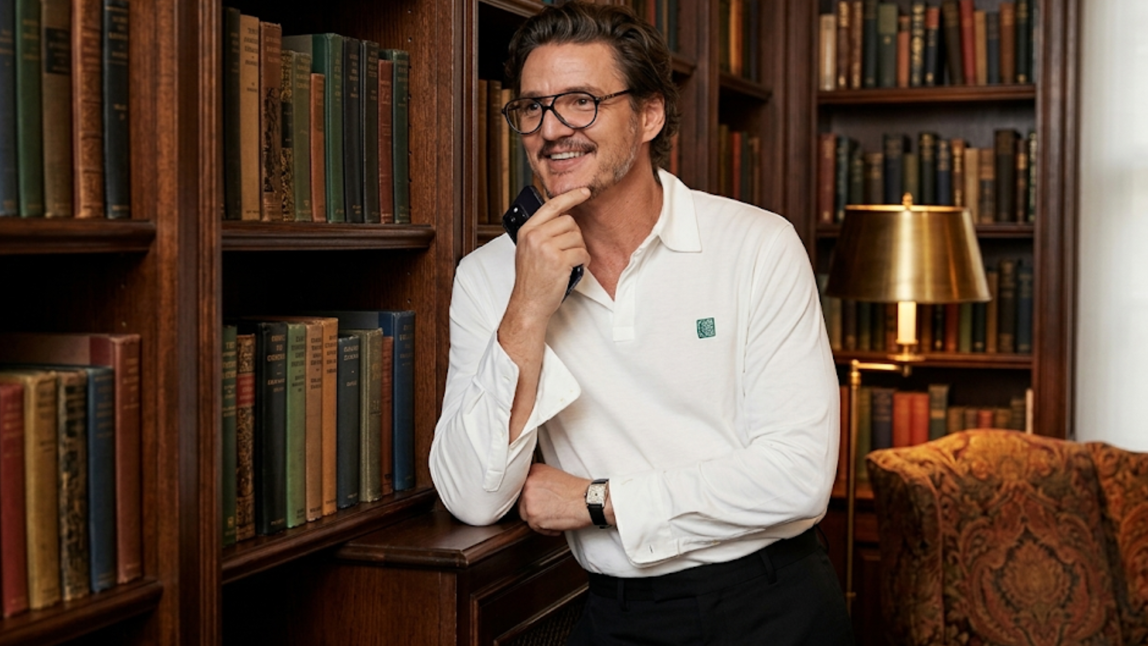 Pedro Pascal wearing a white long sleeve polo shirt on The Late Show with Stephen Colbert, featuring a minimal embroidered chest logo and styled with black trousers and glasses