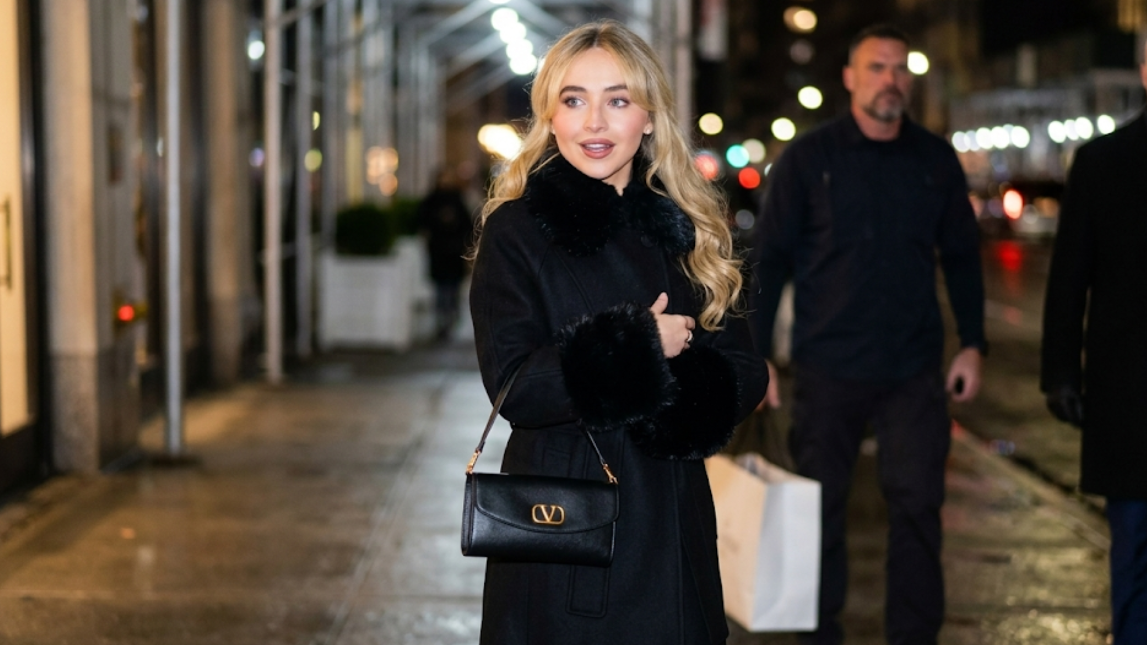 Sabrina Carpenter NYC 2026 black wool coat with faux-fur collar, fur-trimmed cuffs, and double-breasted longline silhouette