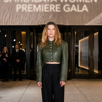 Betty Gilpin NYC 2026 olive green cropped leather jacket with puff shoulders and gold buttons paired with elegant wide-leg trousers