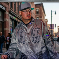 Cookin Soul Italian Hustler silver varsity jacket with metallic finish, collegiate patches, and oversized streetwear silhouette
