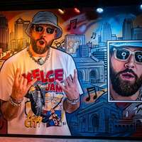 Travis Kelce Jam White T-Shirt featuring comic-style “KELCE JAM” graphic with bold red, blue, and yellow streetwear design on cream base