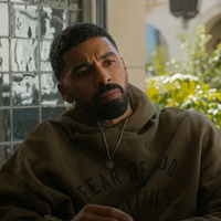Olive green Fear of God Essentials hoodie inspired by Nemesis Season 1 Isaiah Stiles character, featuring a relaxed fit, minimalist streetwear design, and pullover silhouette styled in cinematic fashion.