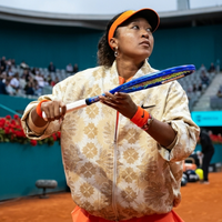 Naomi Osaka wearing a custom Nike cream bomber jacket with gold geometric patterns and neon orange detailing at Madrid Open 2026 warm-up courtside.