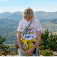 The Four Seasons S02 Kerri Kenney Buck N’ A Beer T-Shirt styled in an indie outdoor aesthetic featuring vintage deer illustration, earthy tones, and layered accessories with light-wash denim.
