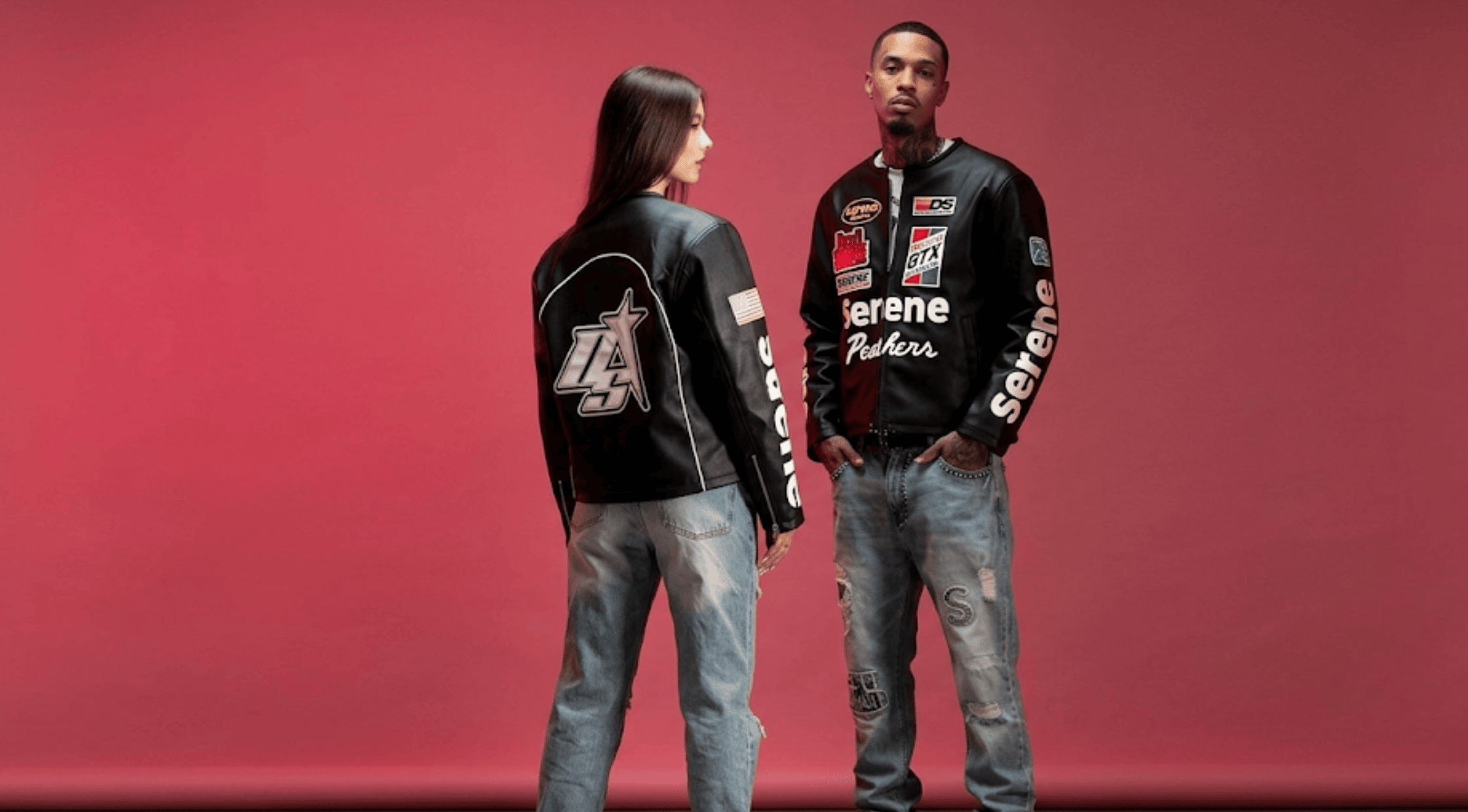 A man and a woman standing together in matching Serene GT black leather racing jackets with bold graphic patches against a dark pink backdrop.